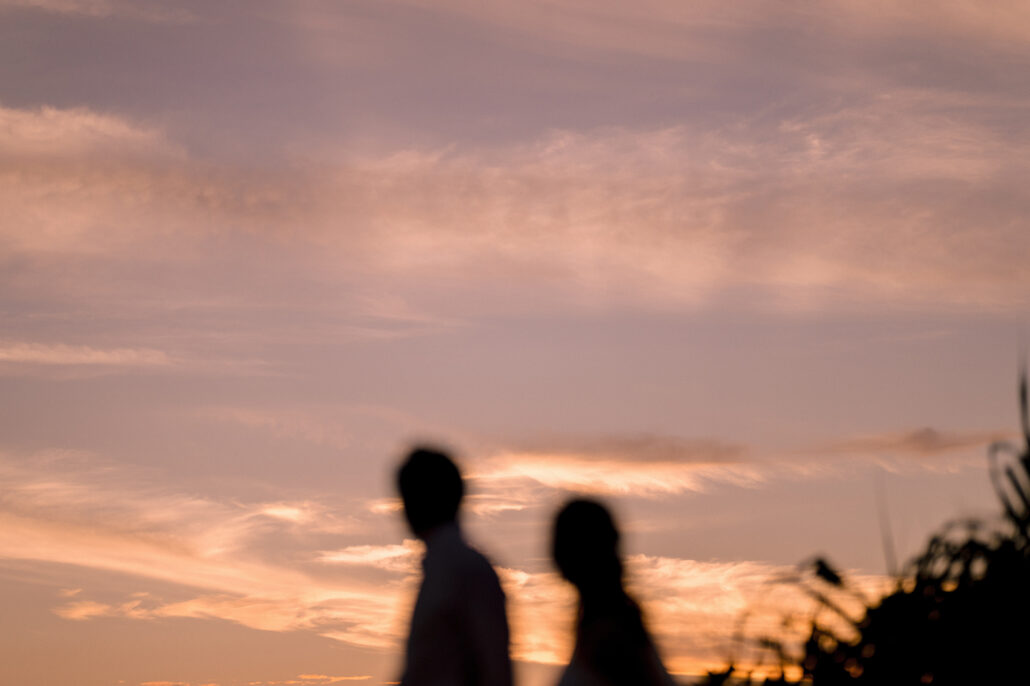 Two figures in silhouette walk along a ridge against a pink and gold sunset sky.
