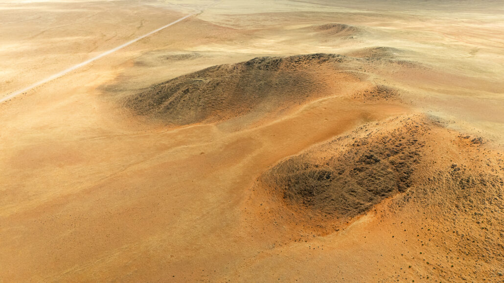 Drone shot of Namibia’s D707 road slicing through untouched desert, revealing wild textures and color shifts.