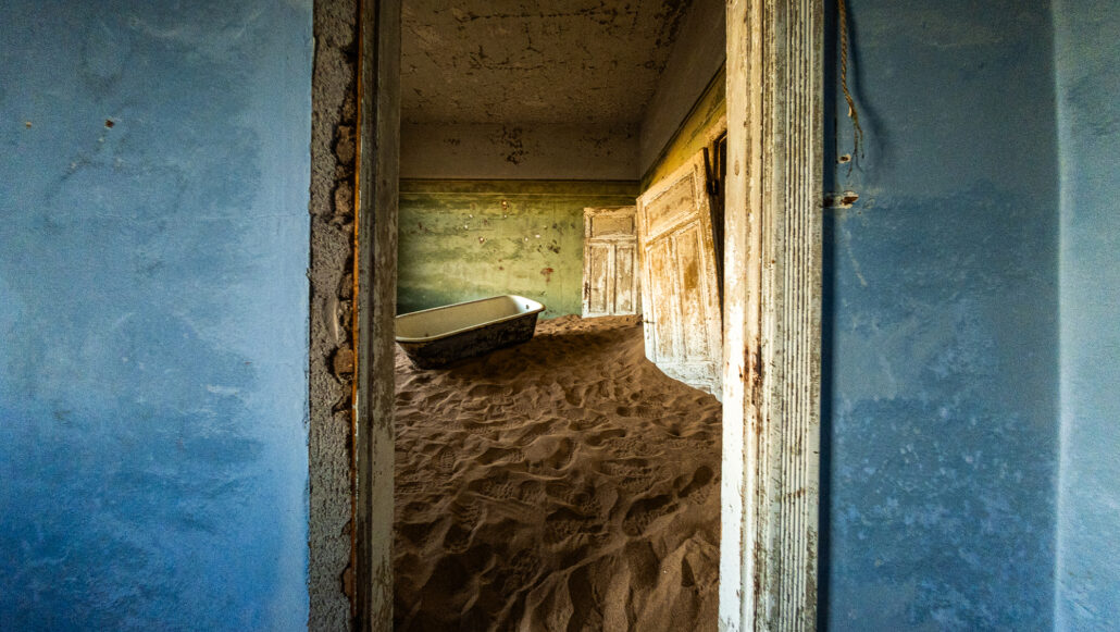 Sunlight casting soft shadows on sand-filled floors of a deserted room in Kolmanskop.