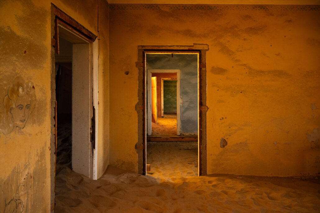 Sunlight casting soft shadows on sand-filled floors of a deserted room in Kolmanskop.