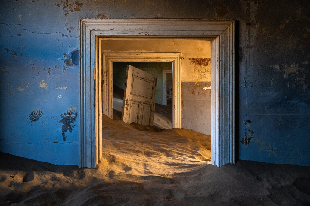 Cracked door hanging open in a house overtaken by sand at Kolmanskop, Namibia.