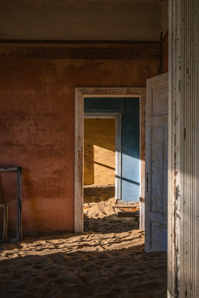 Early morning light streaming through shattered windows in a Kolmanskop hallway.