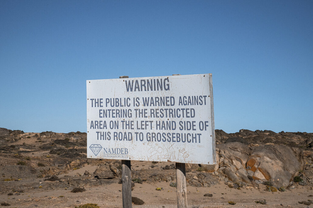 Weathered coastal signs warning travelers to stay on the road in forbidden diamond territory.