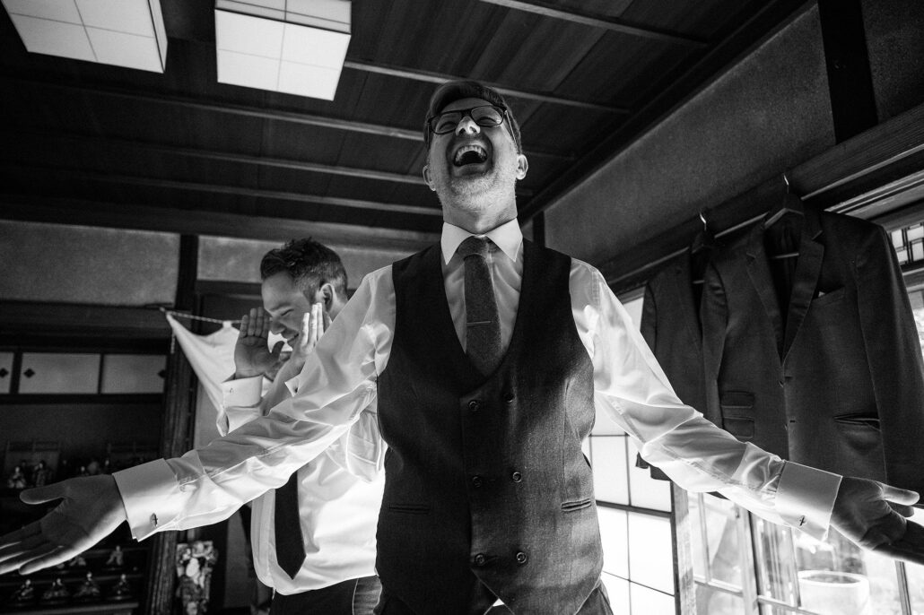 Groom laughing wide in a tatami room, candid getting-ready in traditional Japanese house, documentary wedding coverage.