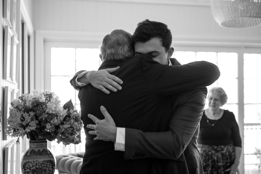 Groom embraces grandfather by sunlit window, authentic multi-generational moment, personal narrative.