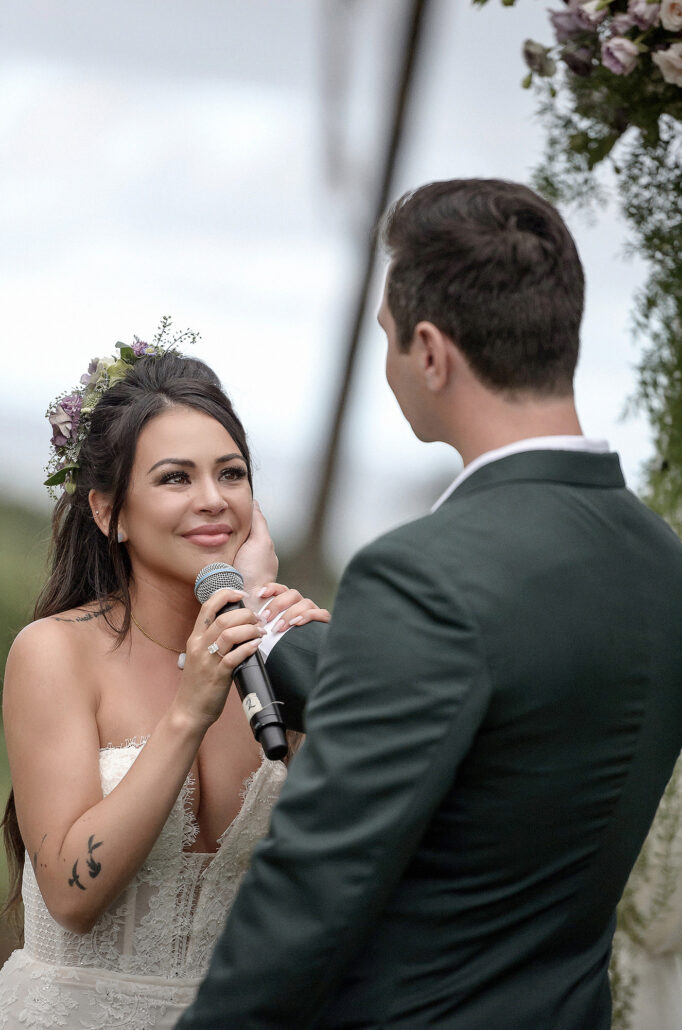 Bride reading vows at an outdoor ceremony in Hawaii, groom cupping her cheek, tearful smile, documentary wedding photography. The celebrity wedding of Janel Parrish from Pretty Little Liars.