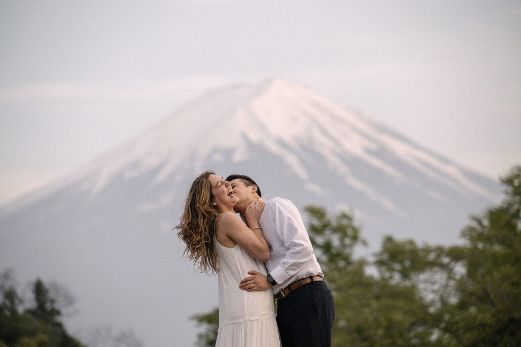 Engaged couple laughing with Mt. Fuji in the background, enhanced using AI editing software for photographers for destination wedding photography in Japan.