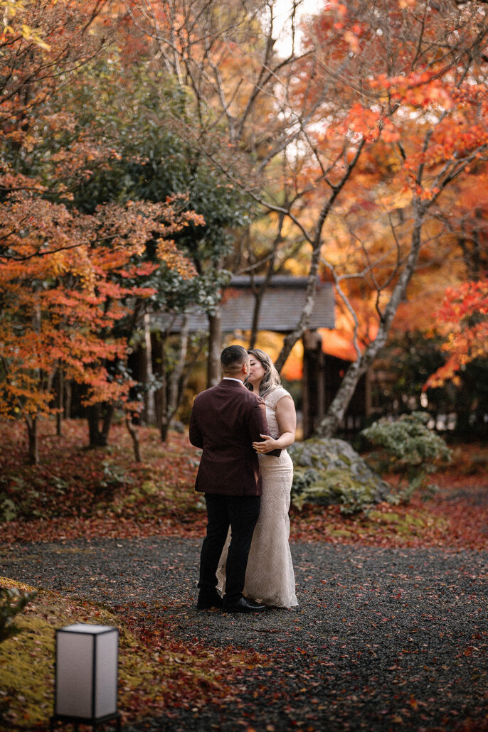 A private garden wedding in Kyoto in Fall. The couple kissing under fiery maple leaves.