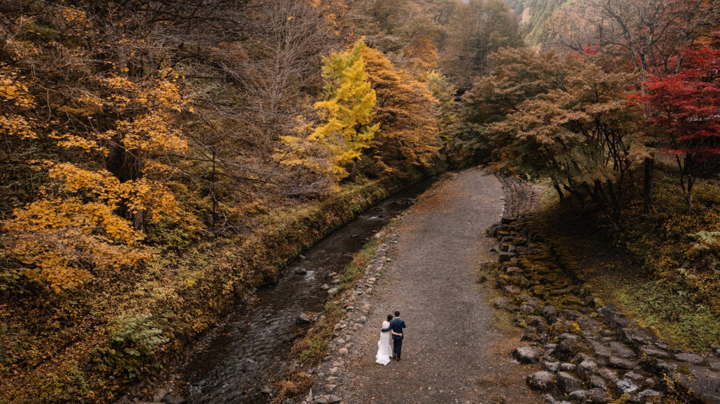 A couple eloping in Japan in the Fall season. In the mountain town of Kosuge in Yamanashi. They are riverside and the tree colours are vibrant.