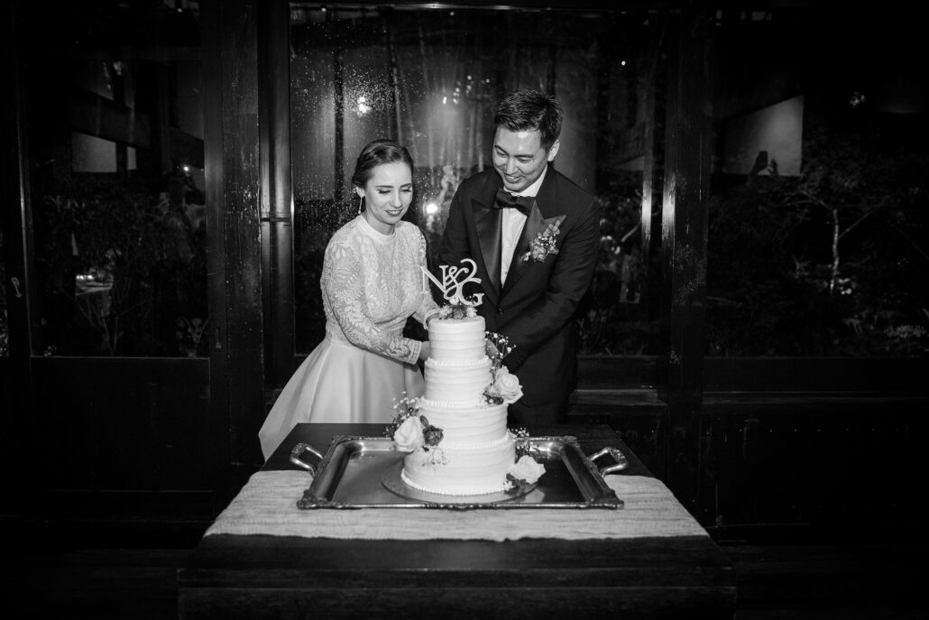 In black and white, the bride and groom cut their tiered wedding cake together at their ryokan wedding reception.