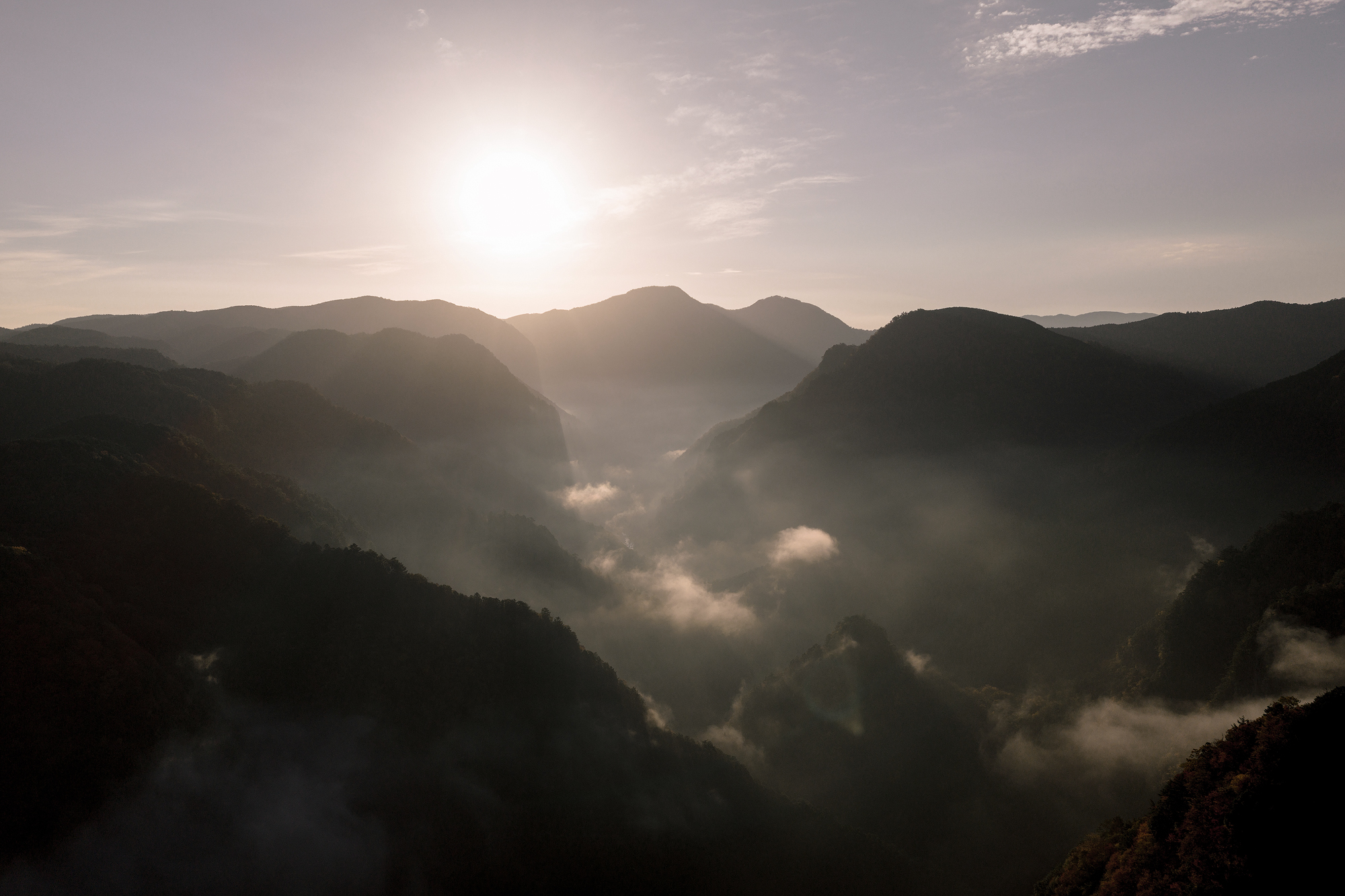 The sun over layered mountains and drifting mist on the border of Nara and Mie, the setting for a Japan elopement in autumn.