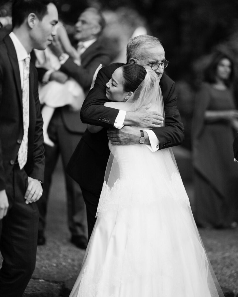 In black and white, the bride closes her eyes as she hugs a guest at a destination wedding in Japan.