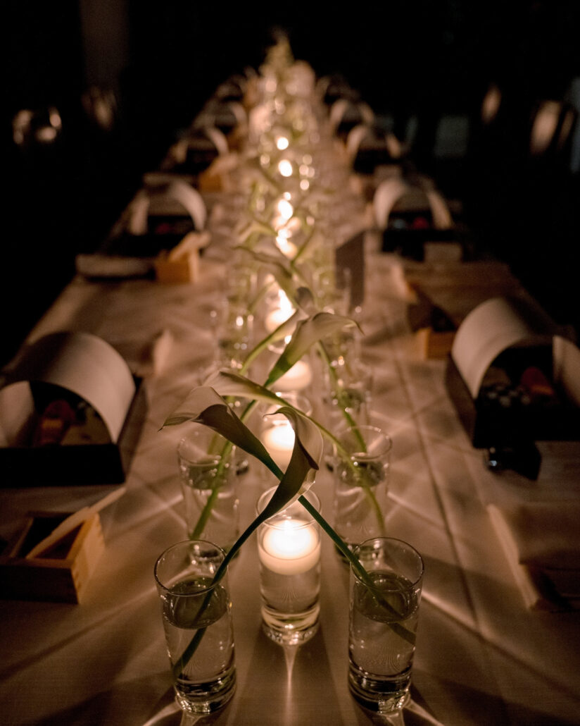 Candlelight and calla lilies run down the long reception table, place settings on either side, at a Greek and Japanese wedding in Japan.