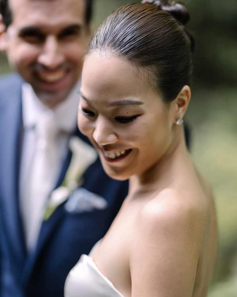 The bride smiles down in a close portrait as the groom laughs behind her in the garden at their Jinya Ryokan wedding.