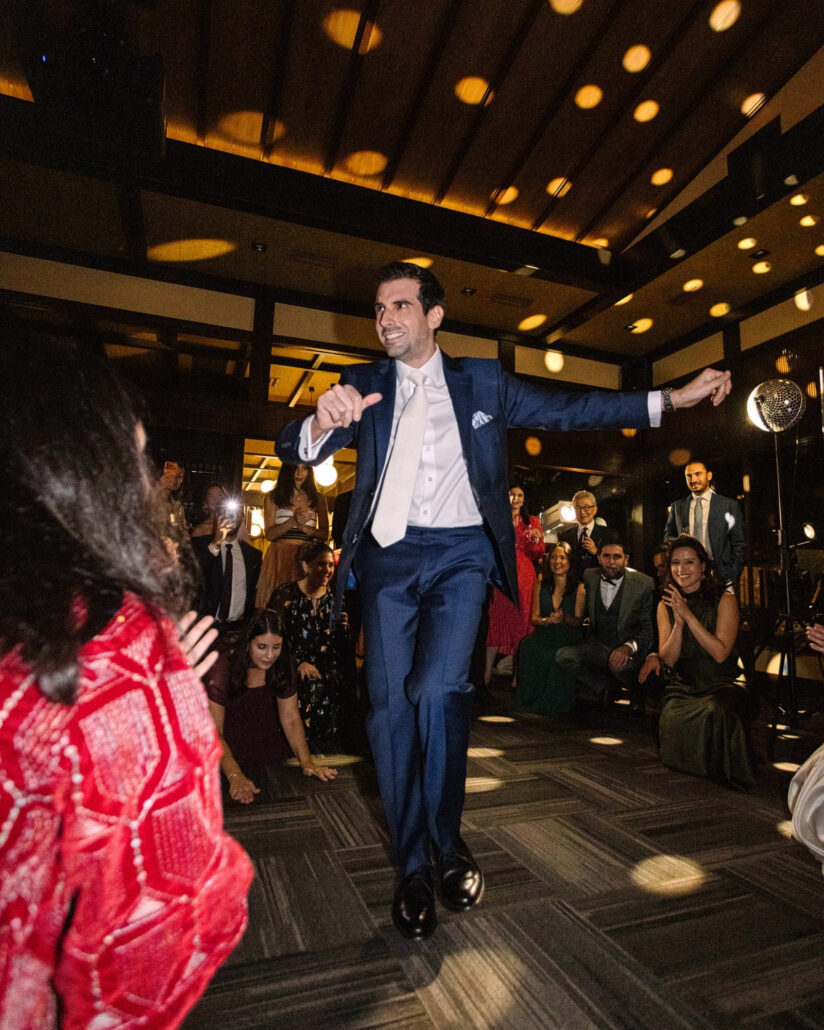 The groom dances into the circle as guests clap and kneel around him during the Greek dancing at a destination wedding in Japan.