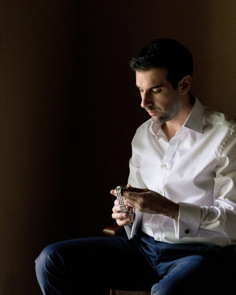 The groom sits in soft window light holding his watch as he gets ready for his destination wedding in Japan at Jinya Ryokan.