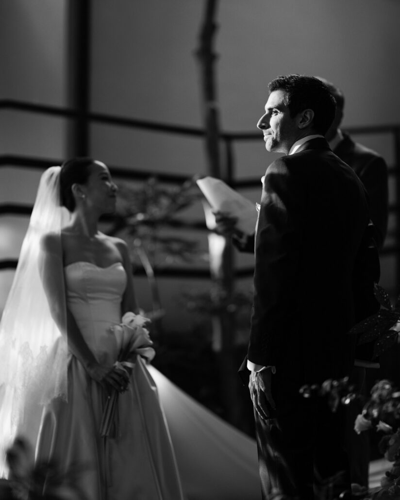 In black and white, the bride looks up at the groom as the vows are read during their garden ceremony at Jinya Ryokan.