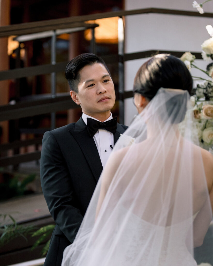 The groom looks at the bride, seen from behind in her long veil, as they face each other at the altar of their ryokan wedding ceremony in Japan.