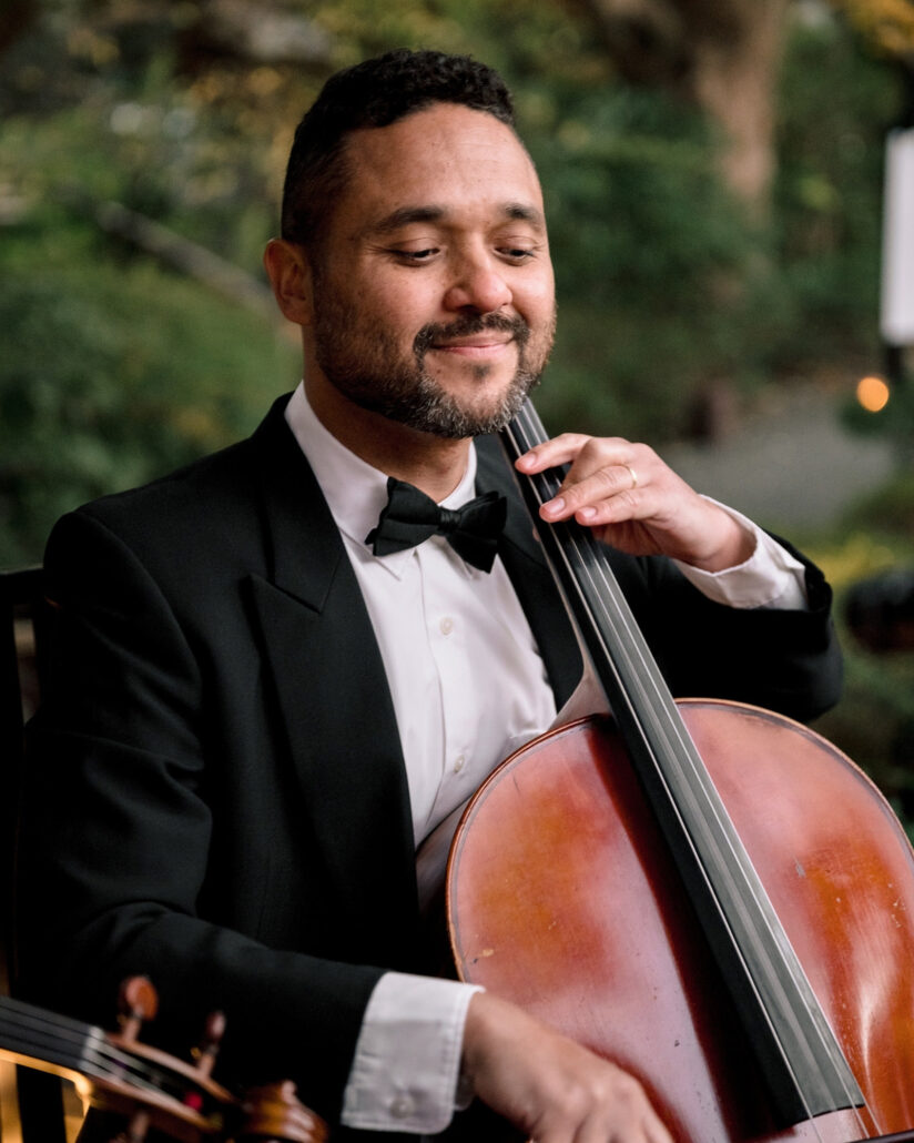 A cellist in a tuxedo smiles as he plays in the garden at a luxury destination wedding in Japan.
