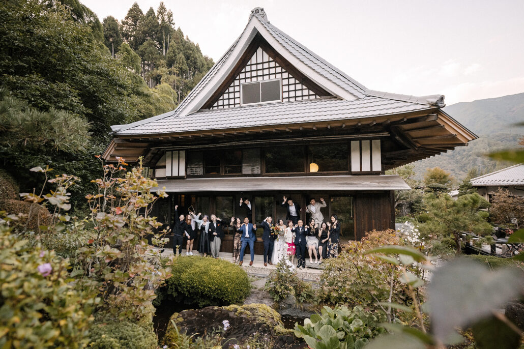 The couple and their guests cheer on the veranda of a traditional Japanese house in the mountains, framed by garden flowers.