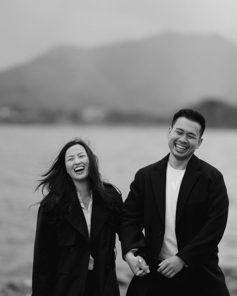 The newly engaged couple laugh hand in hand by one of the Fuji Five Lakes, her hair blowing in the wind, in black and white.