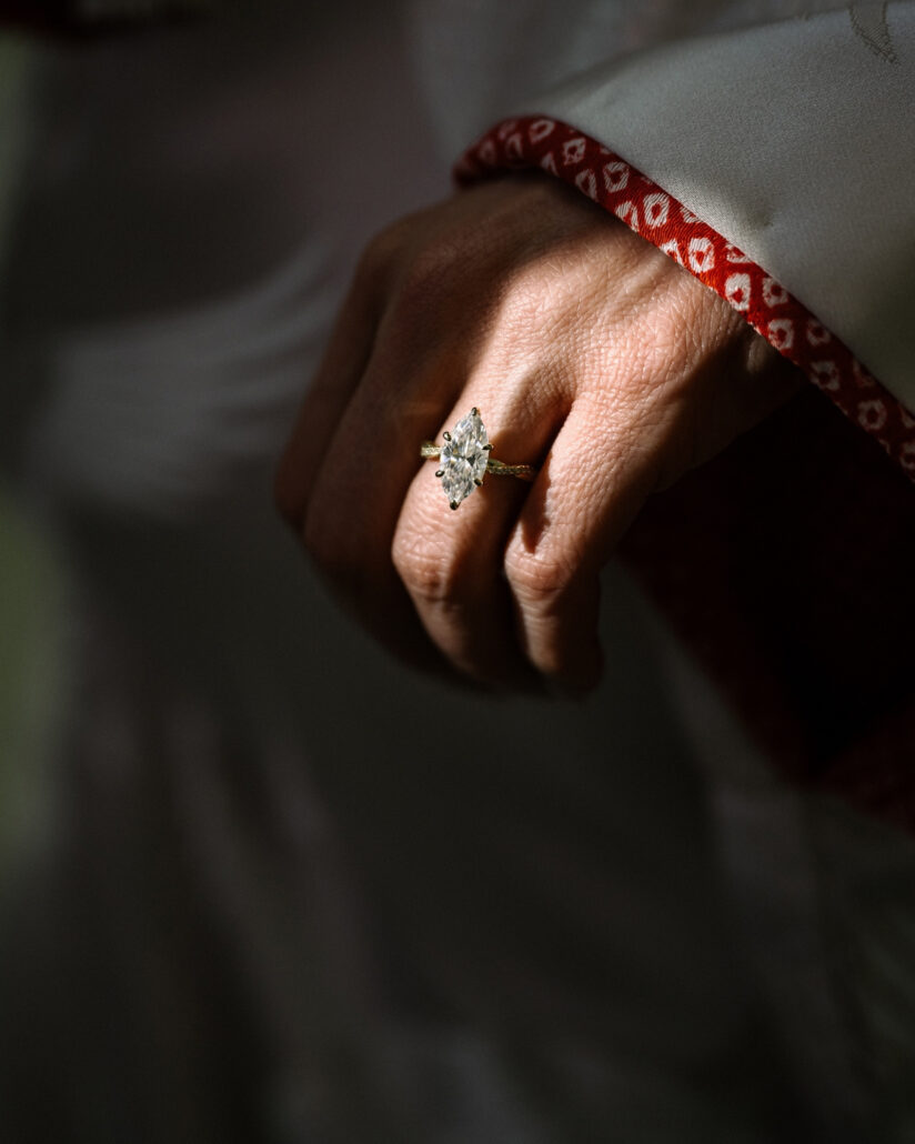A marquise diamond engagement ring sits on the bride's hand as it rests against the red patterned cuff of her white wedding kimono.