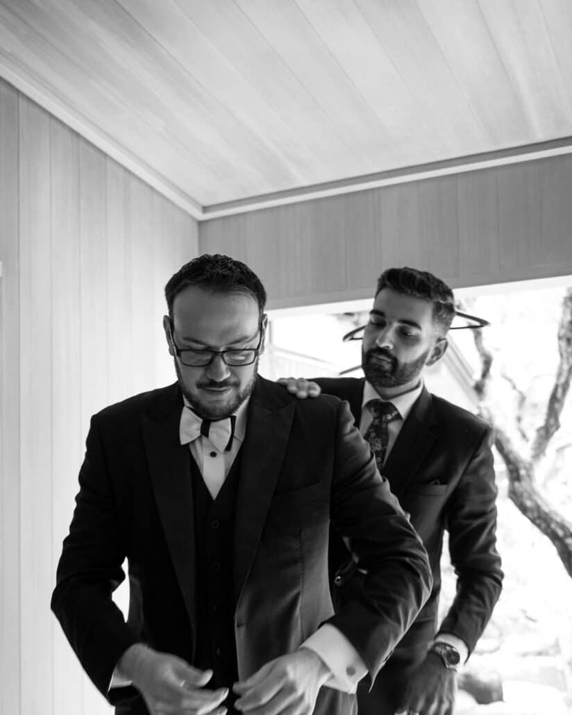 A friend settles the jacket on the groom's shoulders as he buttons it, getting ready for an intimate wedding at a ryokan in Shuzenji.