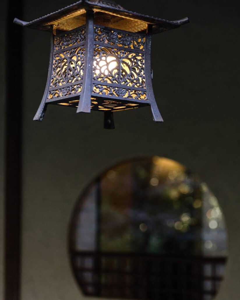 A pierced iron lantern glows above a round lattice window at Jinya in Hadano, the setting for this elopement at a ryokan.