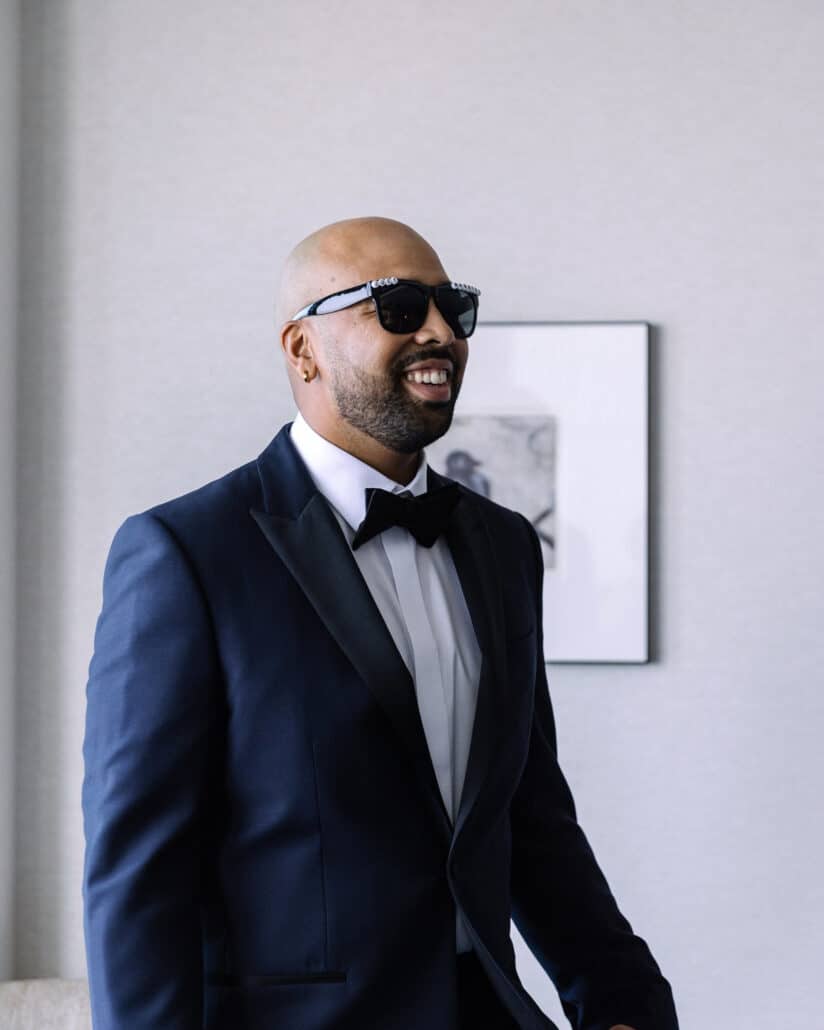 The groom, smiling in his navy tuxedo and black sunglasses, in his hotel room before the Tokyo wedding.