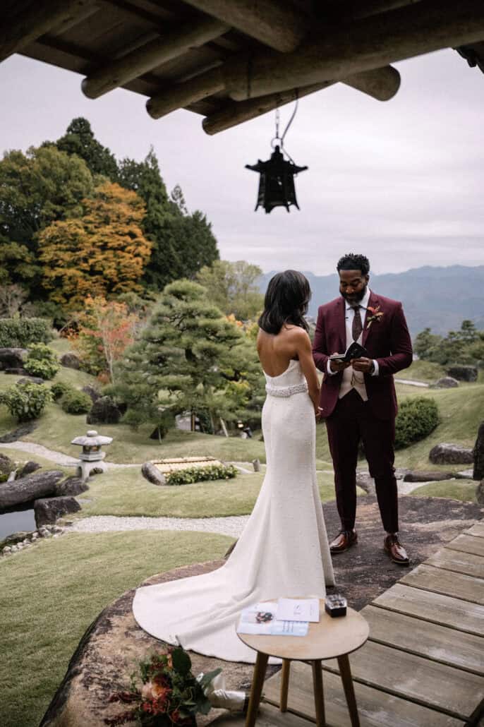 The groom reads his vows under an iron lantern on the wooden terrace, pines and the mountains of Uda behind this Nara wedding for two.