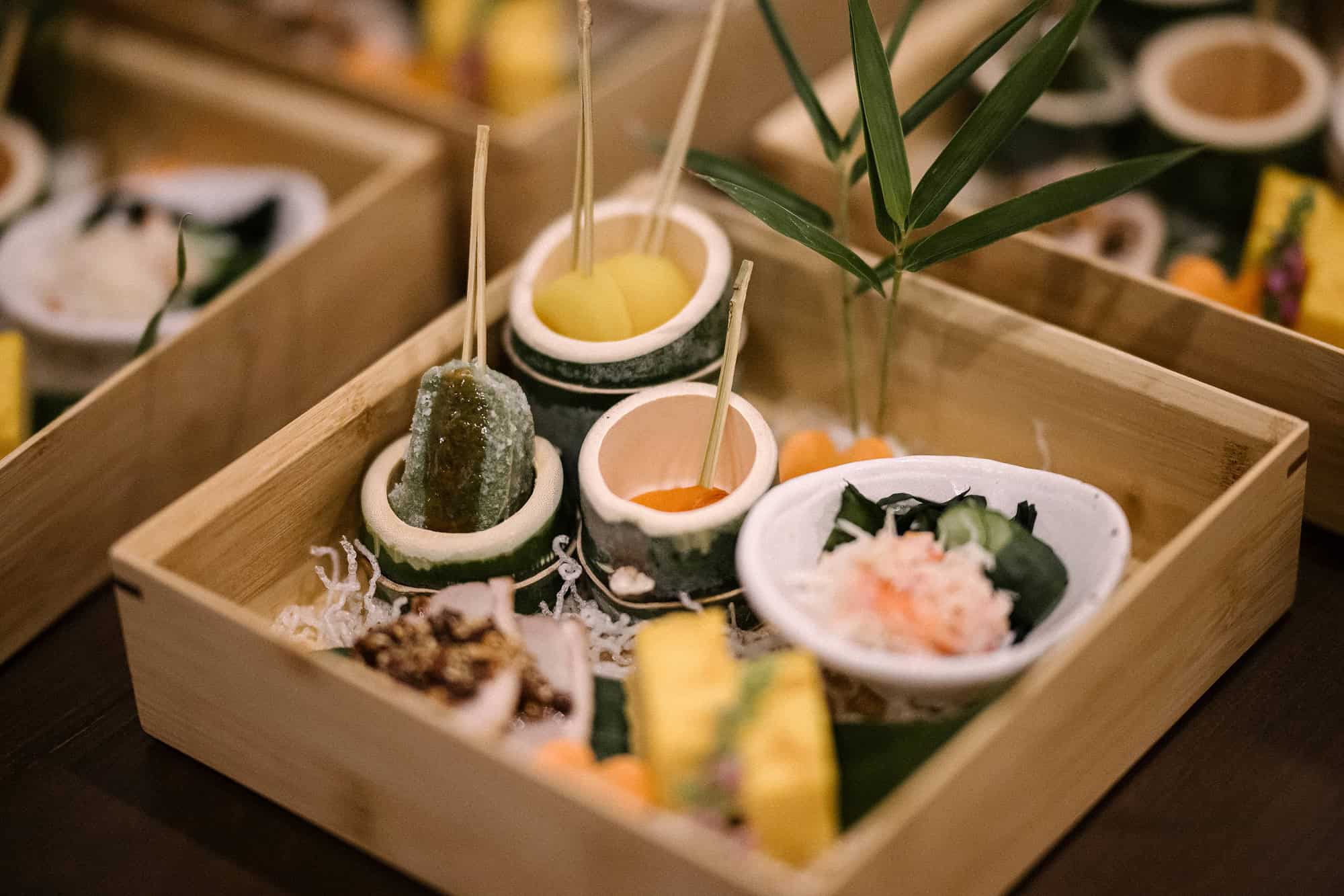 Small seasonal bites in cups cut from green bamboo, set in a wooden box with bamboo leaves, the first course of a Japanese wedding dinner.