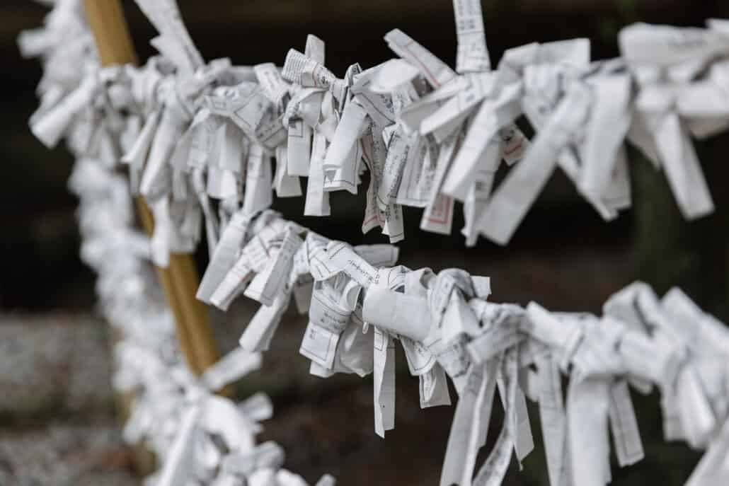Paper fortunes are knotted in rows along ropes at Kawaguchi Asama Shrine, printed Japanese text showing on the folded white slips.