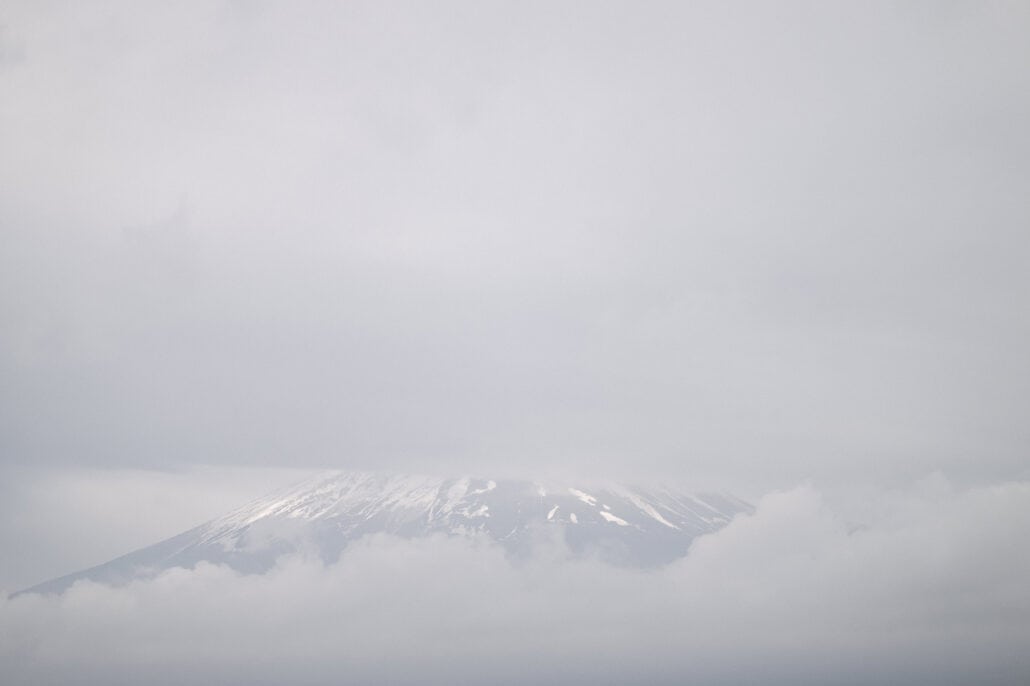 Mt Fuji's snowy upper slopes float between banks of grey cloud, the summit hidden, seen from Lake Kawaguchi in the Fuji Five Lakes.