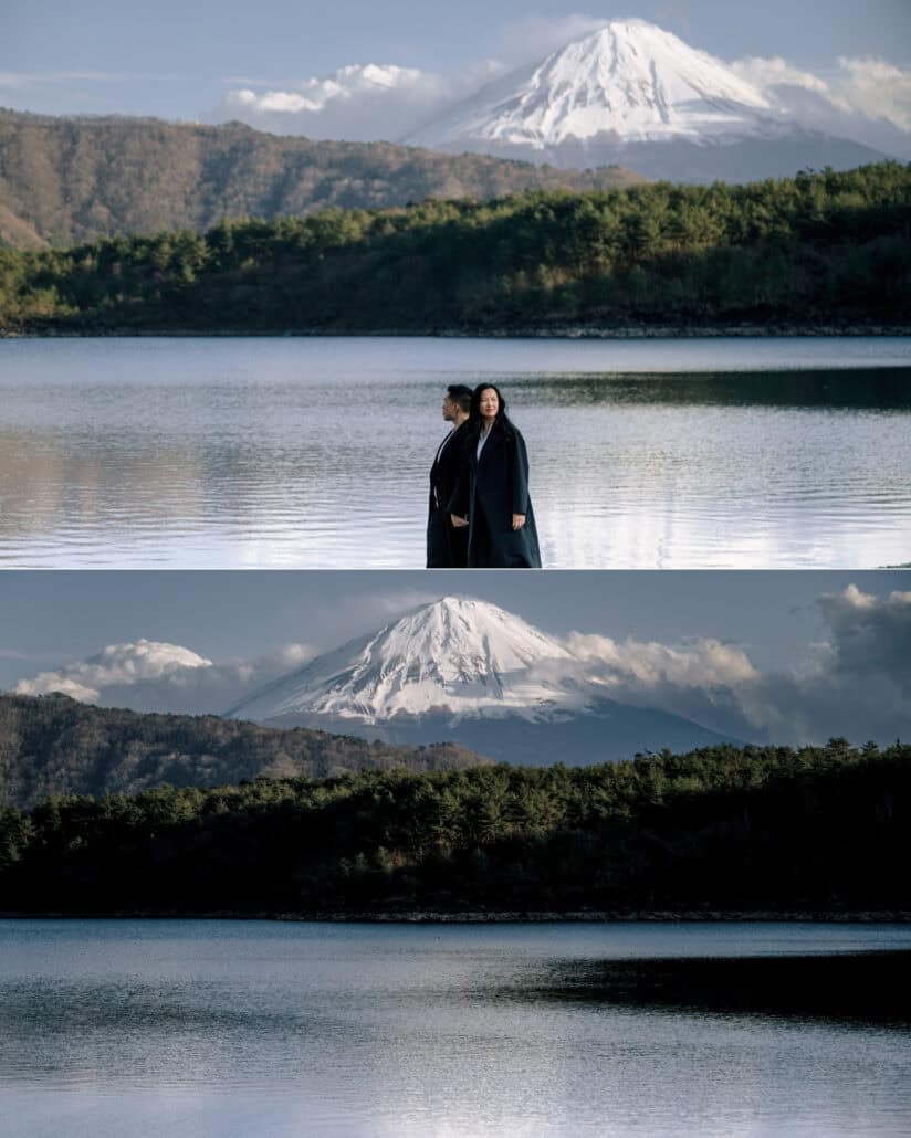 The couple stand at the edge of a still lake below Mount Fuji and a forested ridge, and the mountain alone above the water.