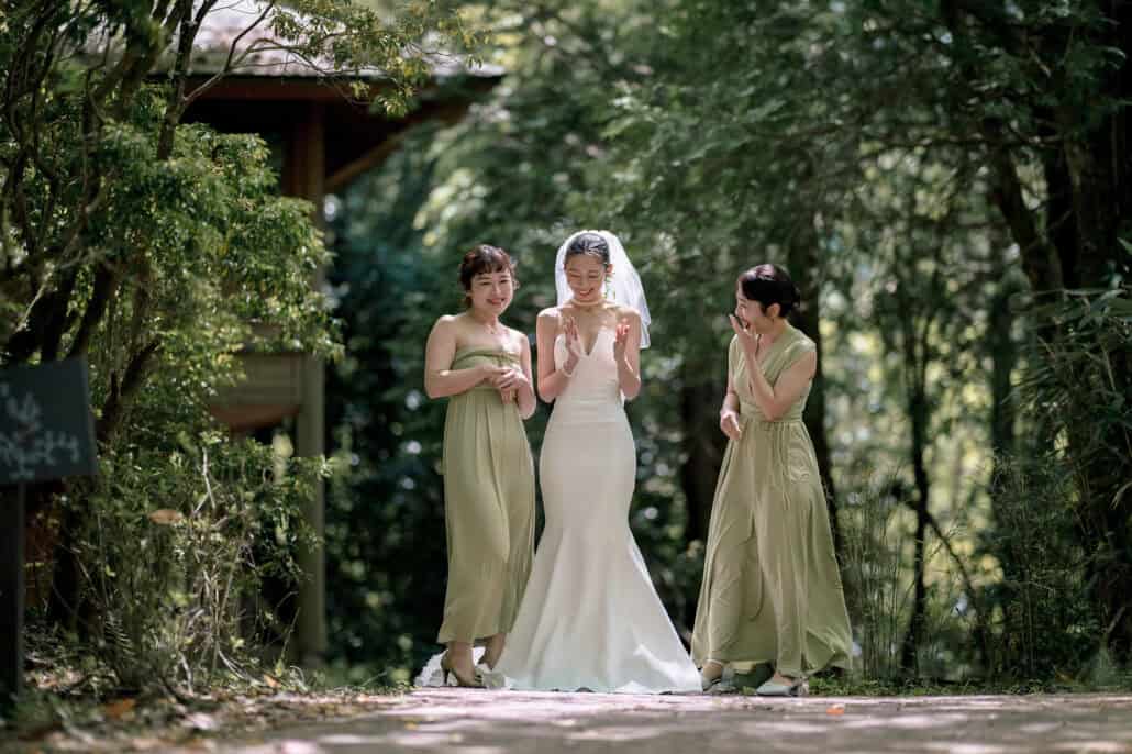 The bride walks a forest path in Hakone with her bridesmaids in sage green, clapping as they go, on the way to her forest wedding in Japan