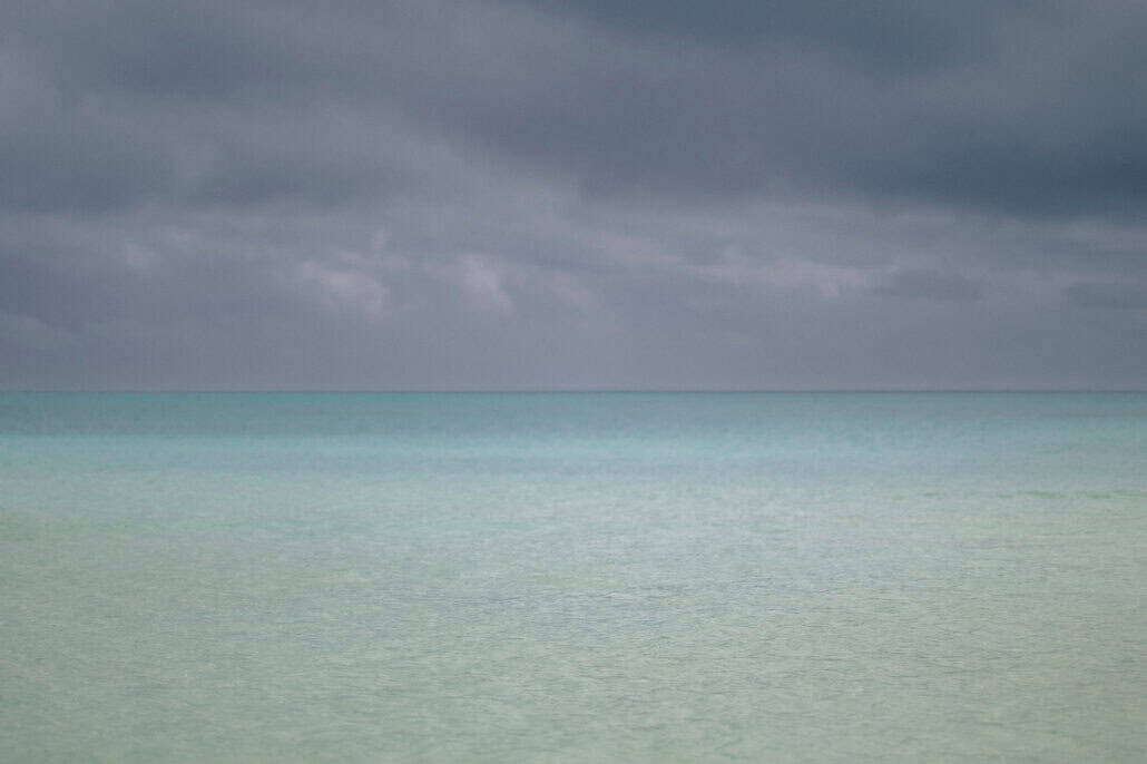 Pale jade shallows run flat to a straight horizon under dark storm cloud off Miyako Island in Okinawa, the afternoon before the wedding.
