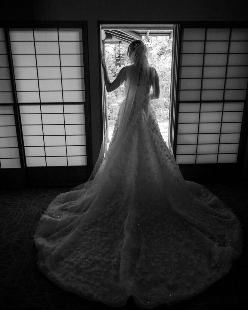 The bride looks out to the garden from a doorway between shoji screens, her long train spread across the floor, on her elopement in Japan.