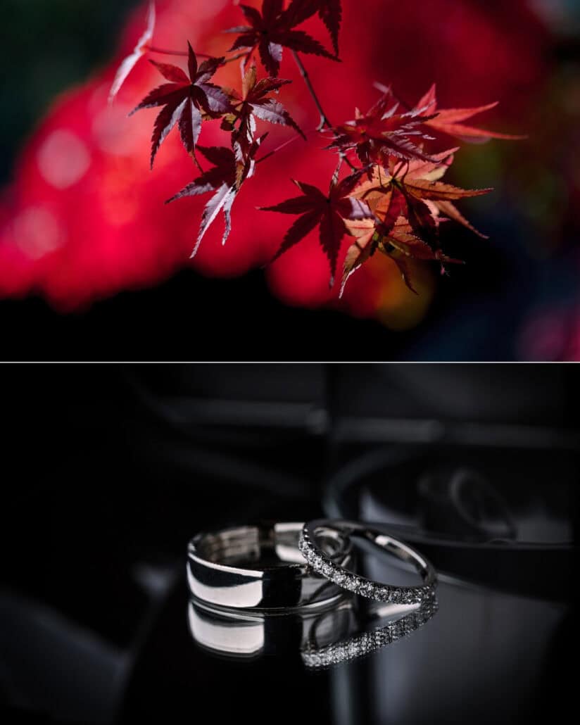 Red maple leaves hang against a red blur in the garden at Jinya, and the two wedding rings rest side by side on a dark reflective surface.