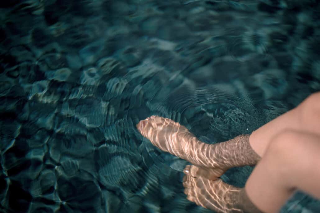 The bride getting ready dips her feet in a pool on the wedding morning, light rippling over dark blue-green water at Rosewood Miyakojima.