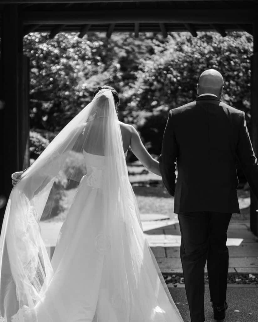 In black and white, the bride and groom step out into the Japanese garden, her long veil and train trailing behind.