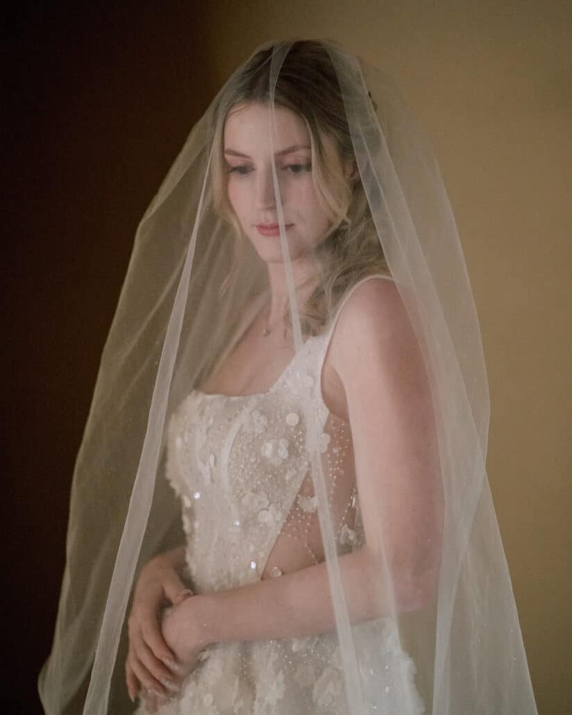 The bride stands under her veil in a beaded floral wedding dress, eyes lowered, in soft light at Jinya before her Japan elopement.