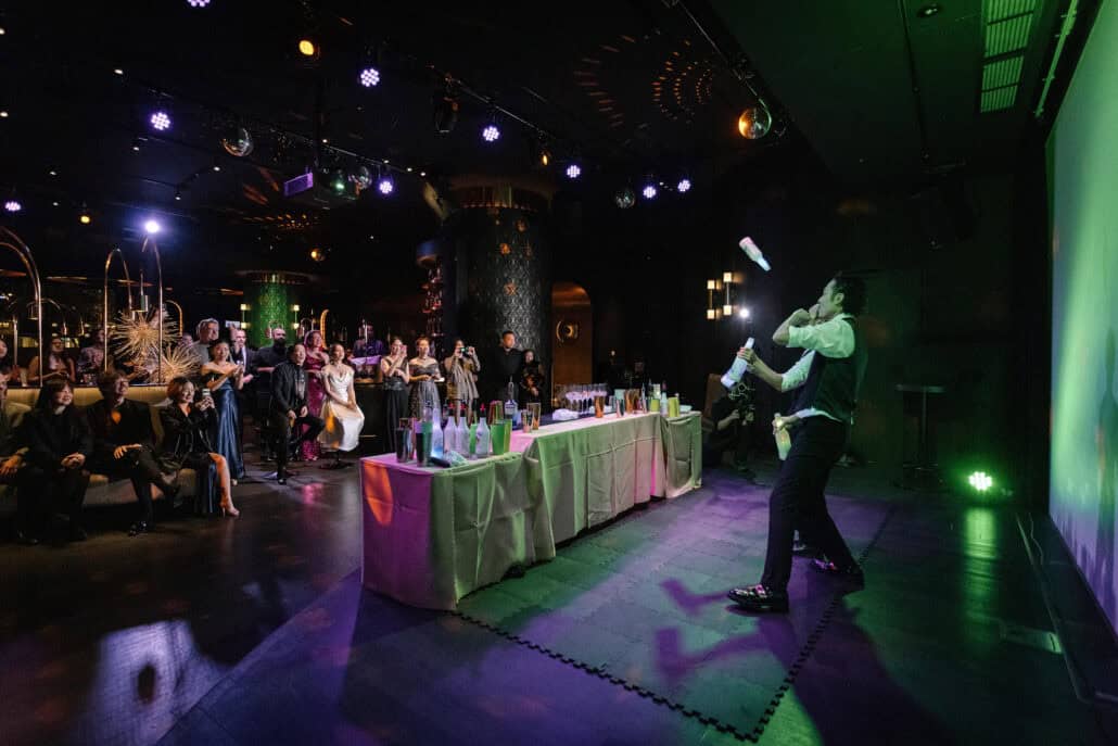 A bartender tosses bottles in a flair bartending show as the couple and their guests watch at the wedding reception at BANK30, disco balls overhead.