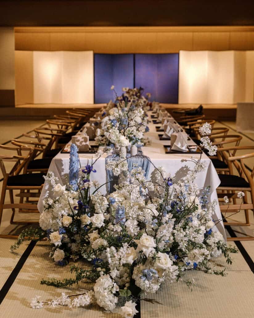 A long table set in a tatami banquet hall at Asaba Ryokan, wishbone chairs on either side and blue and white flowers down its length.
