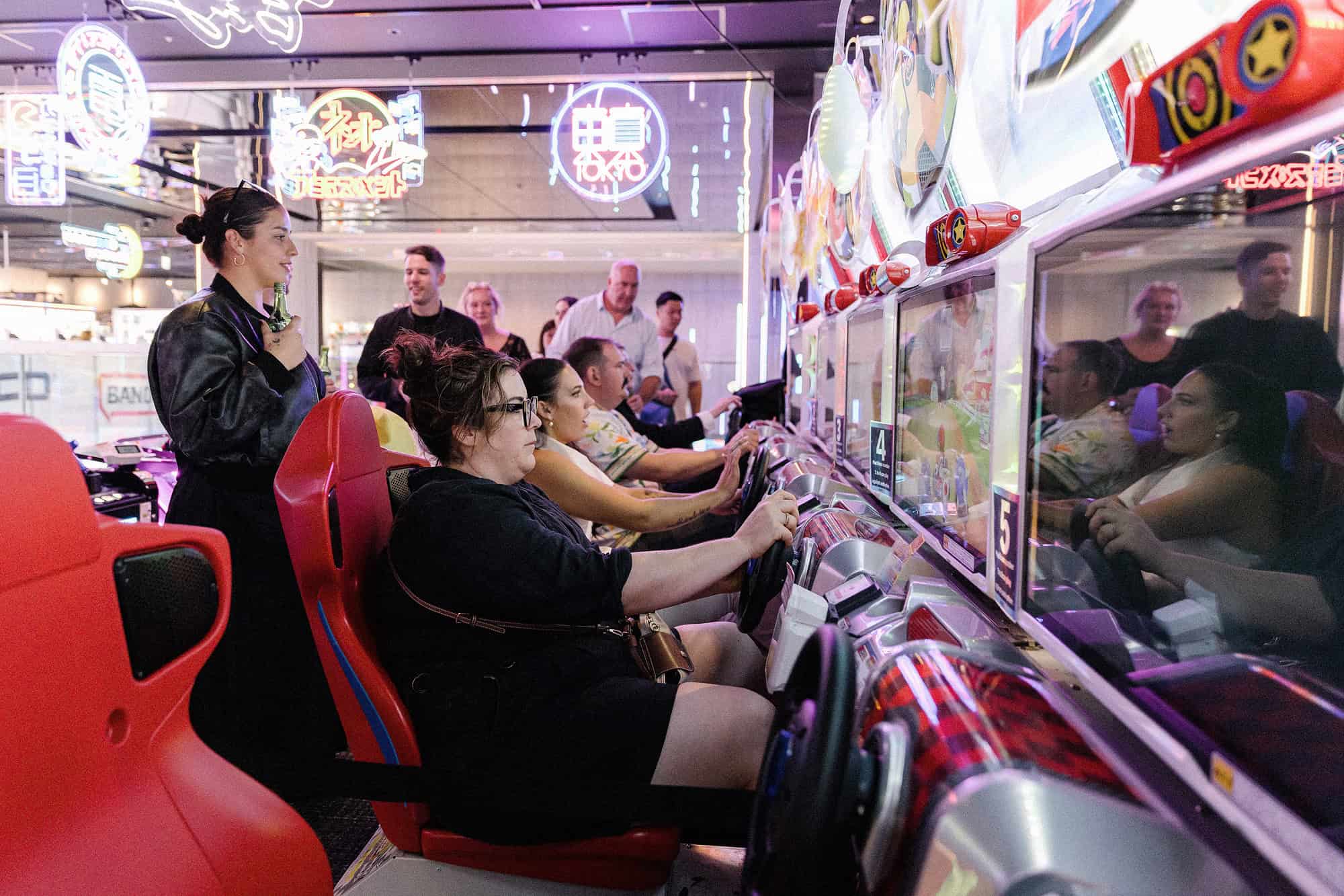Wedding guests and the bride race side by side in red kart seats at an arcade in Kabukicho Tower, Shinjuku, during a wedding after-party in Tokyo.