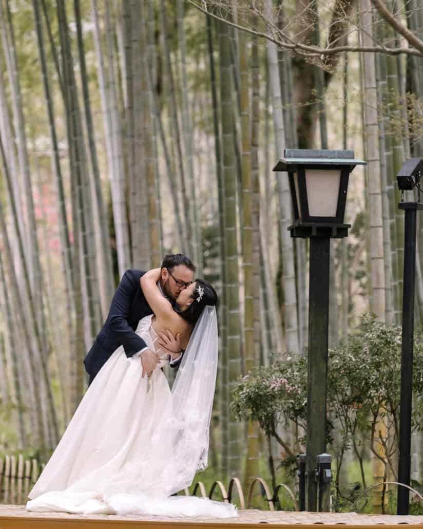 On Shuzenji's bamboo path, the groom dips the bride into a kiss beside a black lantern, tall bamboo rising all around them.