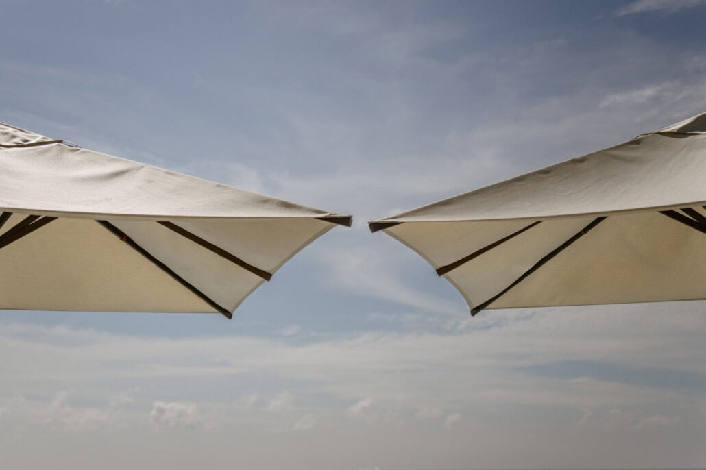 The tips of two cream parasols almost touch against a pale blue sky with light cloud at Rosewood Miyakojima, on the clear afternoon of the wedding.
