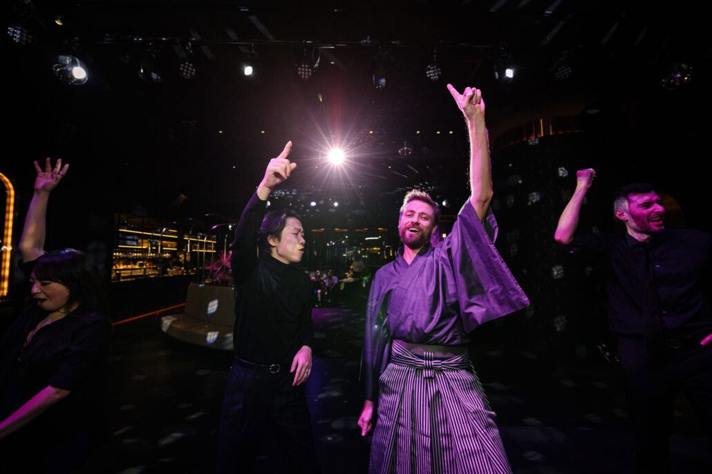 The groom in his black turtleneck and a guest in a dark kimono and striped hakama point to the ceiling on the dance floor at BANK30 in Takeshiba.