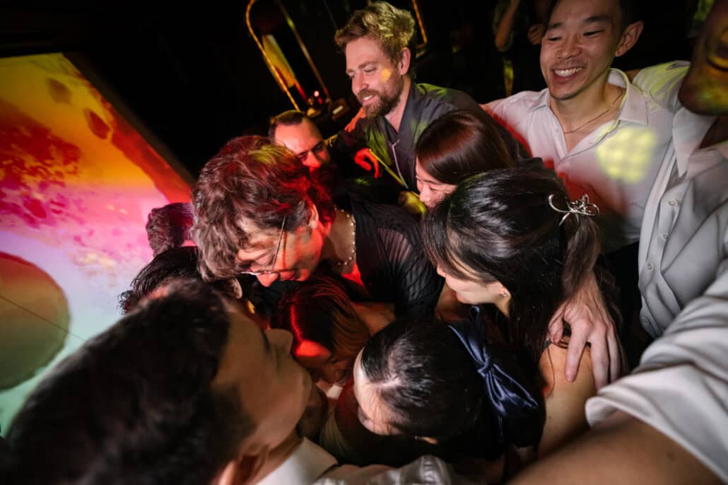 Guests pull into a tight huddle on the dance floor, one in a dark kimono holding a glow stick, late in the wedding after party at BANK30.