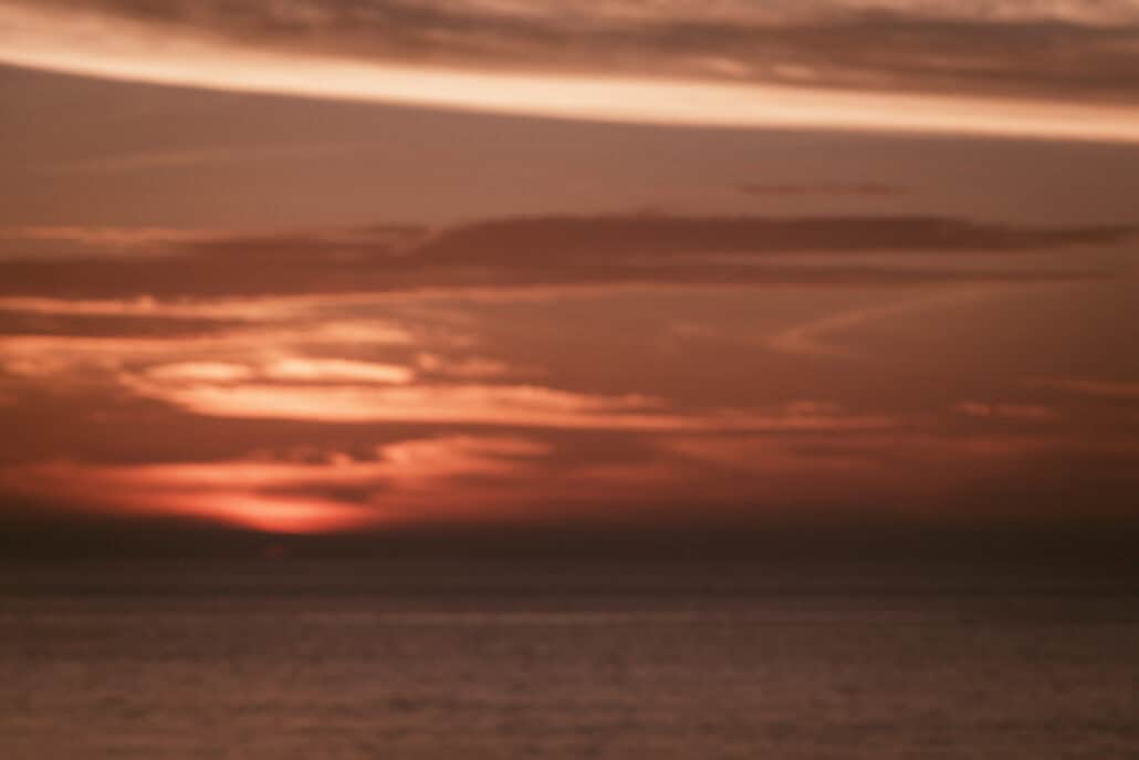 A soft, deep red afterglow lingers on the horizon under long bands of cloud as the sun goes down over the sea on the evening of a Miyakojima wedding.