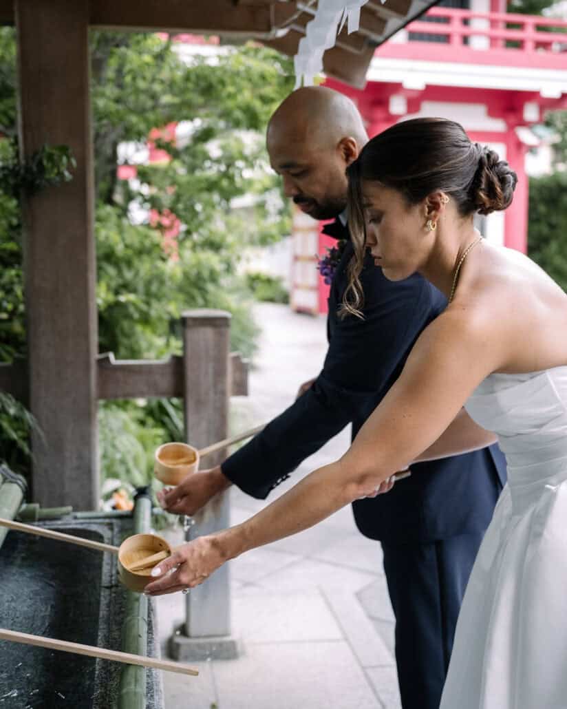 The bride and groom rinse their hands with wooden ladles at the shrine's water basin before their Shinto wedding blessing.